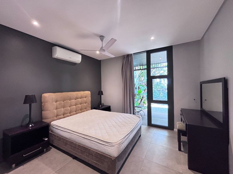 A well-maintained bedroom featuring tiled flooring, a ceiling fan, split-system air conditioning, and direct access to an outdoor patio area through a glass door.