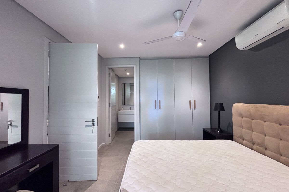 Spacious bedroom featuring built-in cupboards, tiled flooring, a ceiling fan, and an integrated air conditioning unit, with an en-suite bathroom visible.