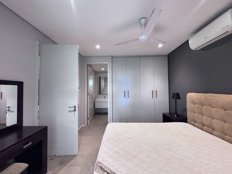 Spacious bedroom featuring built-in cupboards, tiled flooring, a ceiling fan, and an integrated air conditioning unit, with an en-suite bathroom visible.