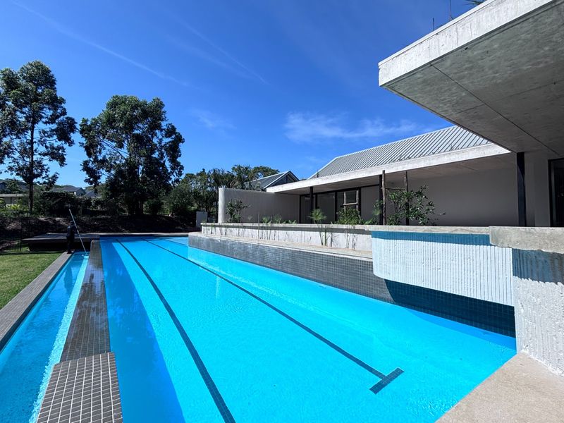 A modern lap pool featuring clean lines, tiled finishes, and a striking concrete cantilevered structure set against a landscaped garden.
