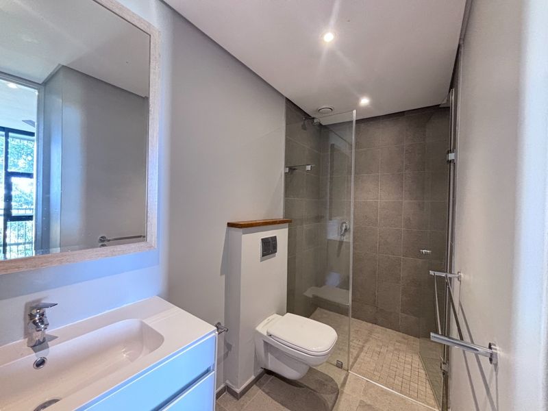 Modern bathroom featuring a wall-mounted toilet, glass-enclosed shower with tiled walls, and a sleek vanity basin with a large mirror.