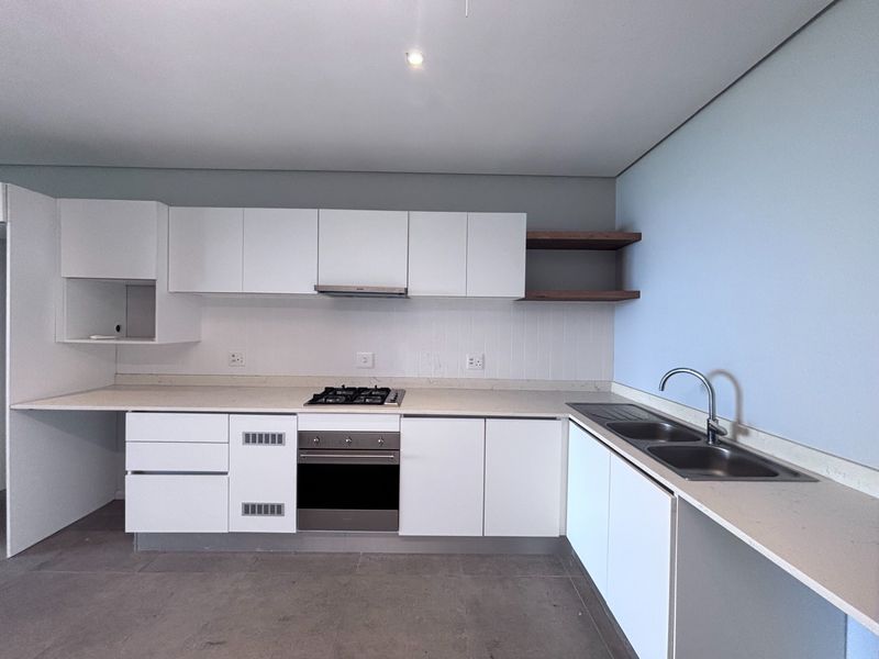 Modern kitchen featuring white cabinetry, stone countertops, gas hob, built-in oven, and double sink with tiled flooring.
