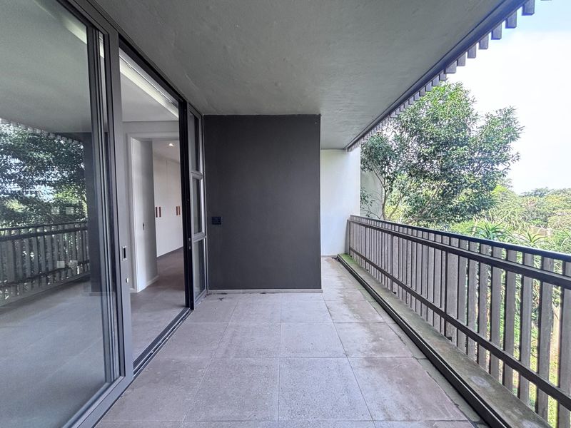 A spacious covered balcony featuring tiled flooring, a metal balustrade, and large sliding glass doors providing seamless access to the interior living space.