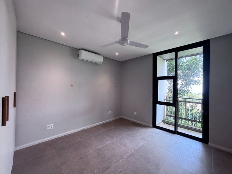A bright, empty bedroom featuring modern tiled flooring, a ceiling fan, split-system air conditioning, and sliding glass doors leading to a private balcony.