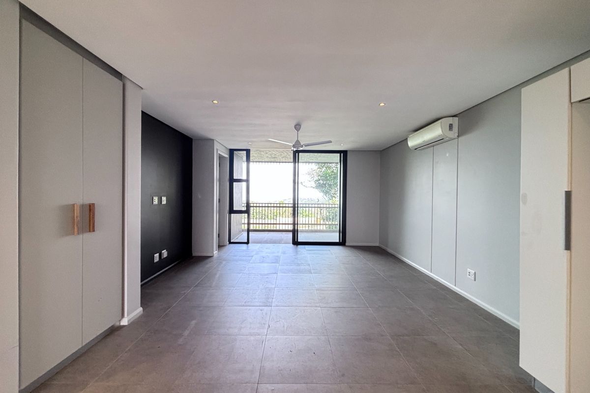 Spacious, modern living area featuring large format floor tiles, built-in storage, air conditioning, and direct access to an outdoor balcony through sliding glass doors.