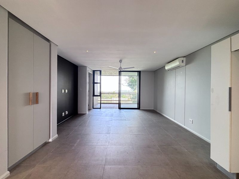 Spacious, modern living area featuring large format floor tiles, built-in storage, air conditioning, and direct access to an outdoor balcony through sliding glass doors.