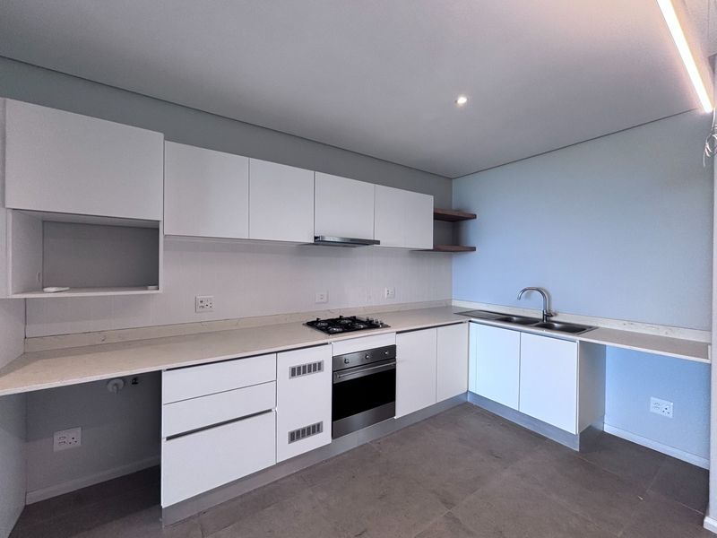 Modern kitchen featuring white cabinetry, stone countertops, integrated gas hob, oven, extractor fan, and a double sink with tiled flooring.