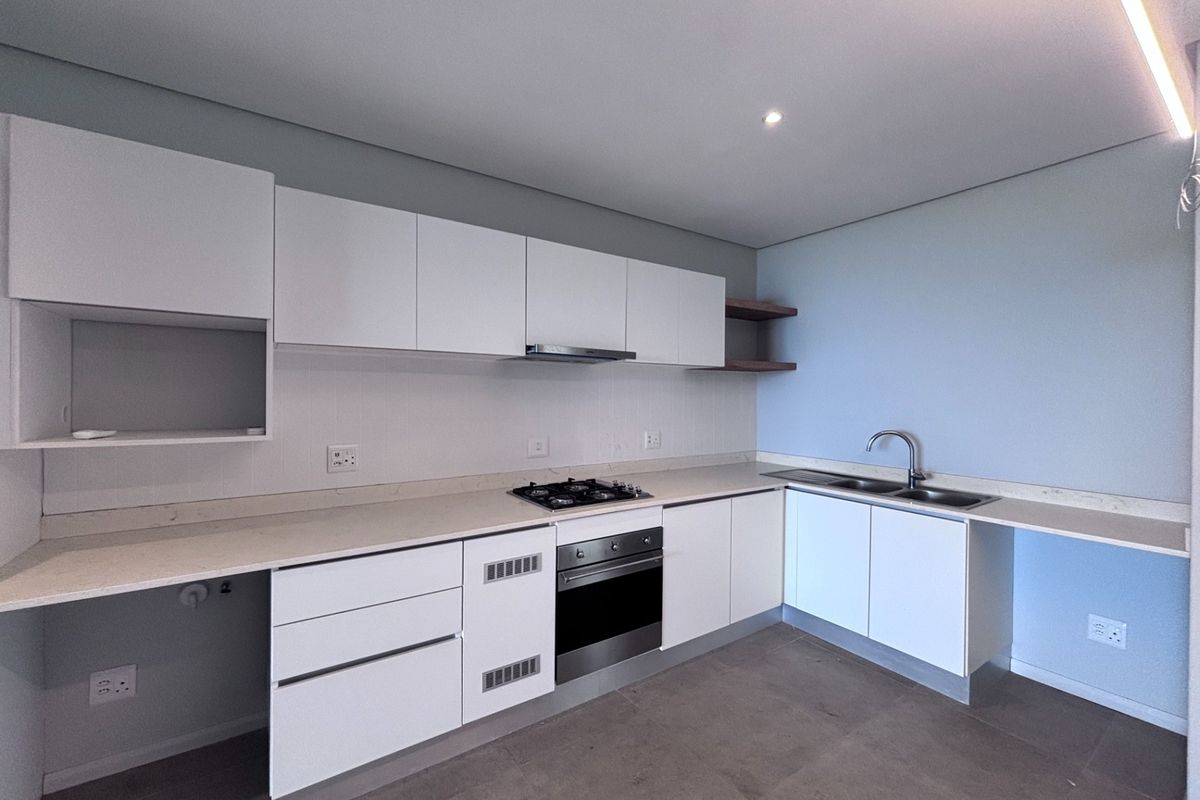 Modern kitchen featuring white cabinetry, stone countertops, integrated gas hob, oven, extractor fan, and a double sink with tiled flooring.