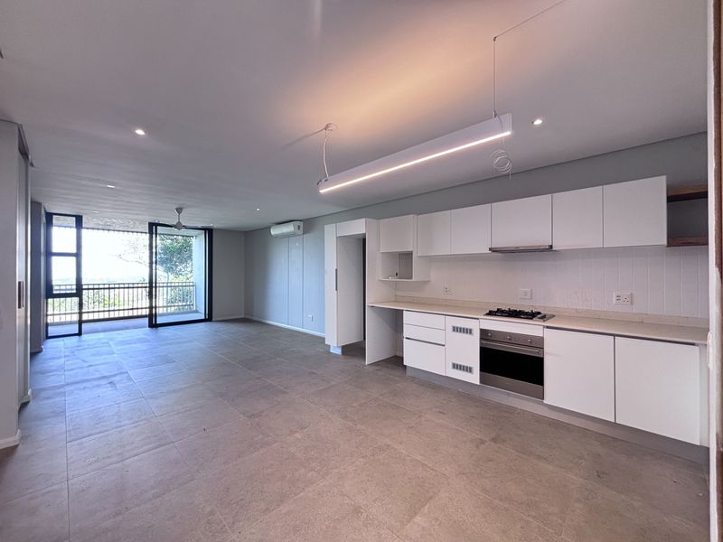 Spacious open-plan living area featuring a modern kitchen with built-in appliances, stone countertops, and seamless access to a private balcony.