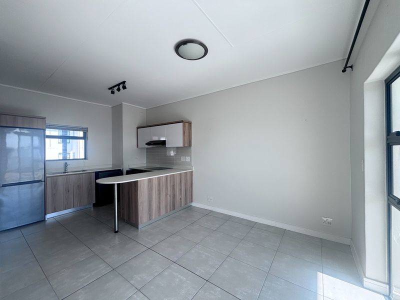 Modern open-plan kitchen and living area featuring neutral cabinetry, a breakfast bar, and tiled flooring in a clean, well-maintained apartment setting.