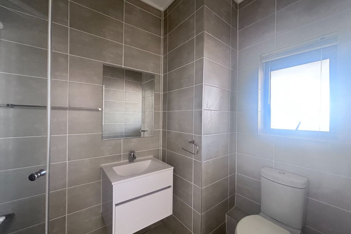 A modern, well-maintained bathroom featuring a wall-mounted vanity, tiled walls, a shower enclosure, and a toilet.