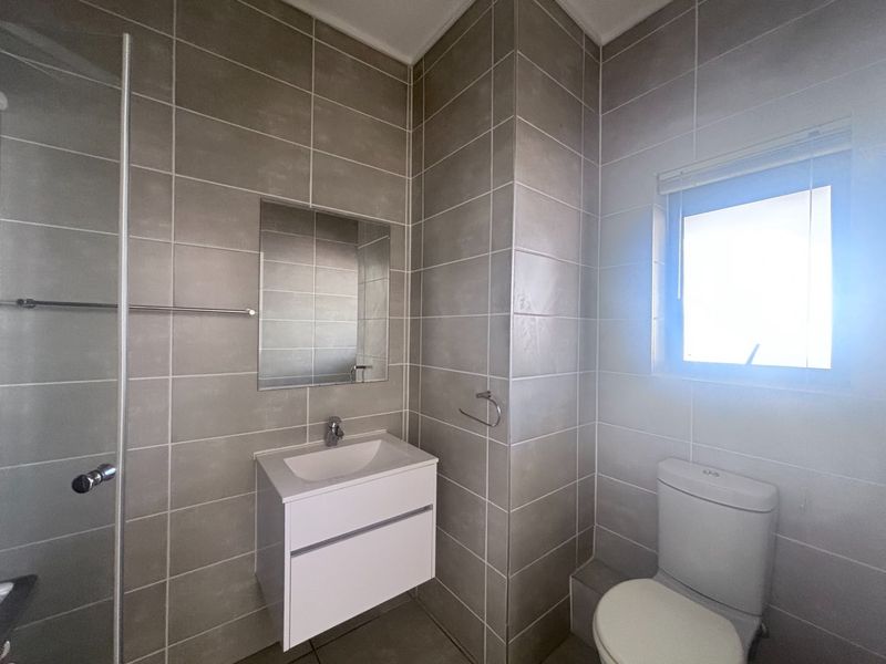 A modern, well-maintained bathroom featuring a wall-mounted vanity, tiled walls, a shower enclosure, and a toilet.