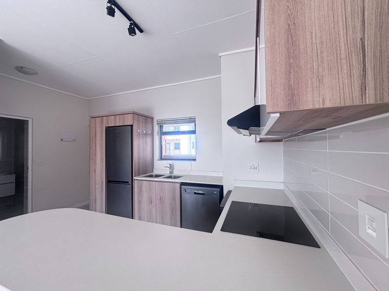 Modern kitchen featuring wood-look cabinetry, light countertops, subway tile backsplash, integrated hob, and extractor fan in a clean, contemporary apartment setting.