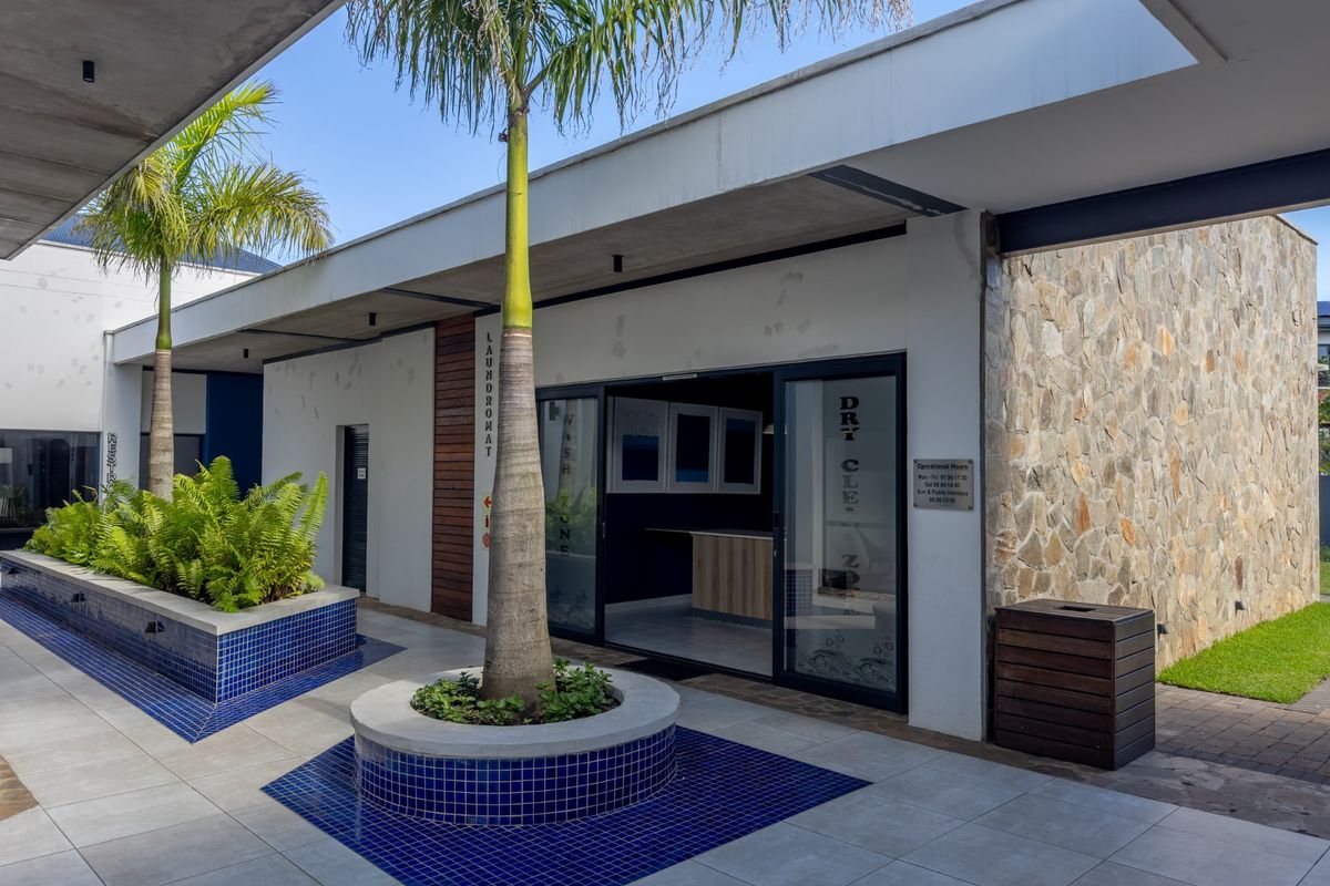 A modern outdoor courtyard area featuring stone-clad walls, tiled flooring, built-in planters, and access to a laundry facility with sliding glass doors.