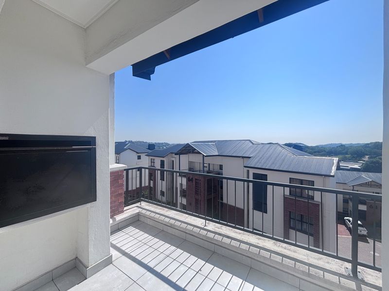 A covered balcony featuring a built-in braai, tiled flooring, and a metal balustrade, offering an elevated view of the surrounding apartment complex.