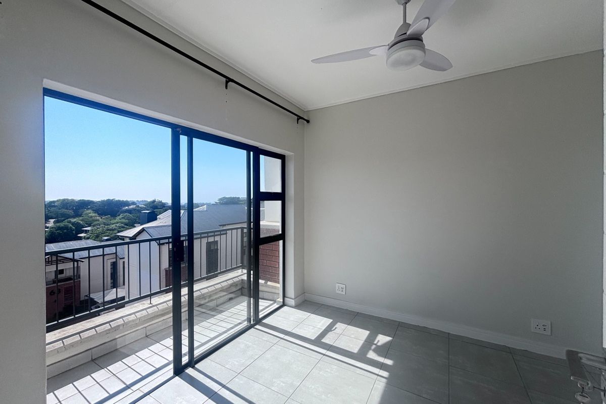 A bright, empty bedroom featuring tiled flooring, a ceiling fan, and a large sliding glass door leading to a private balcony.