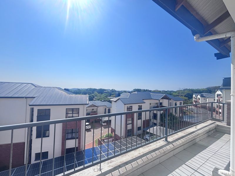 A spacious balcony with metal railings offering an elevated view of the surrounding apartment complex and landscape.