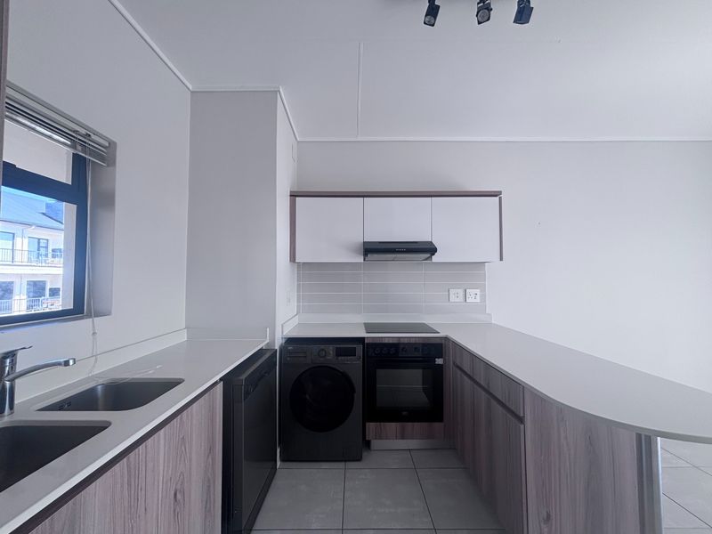 Modern kitchen featuring sleek wood-grain cabinetry, stone countertops, integrated electric oven and hob, and a functional double sink layout.