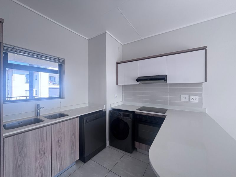 Modern kitchen featuring sleek cabinetry, stone countertops, integrated oven, electric hob, extractor fan, and a double basin sink with tiled flooring.