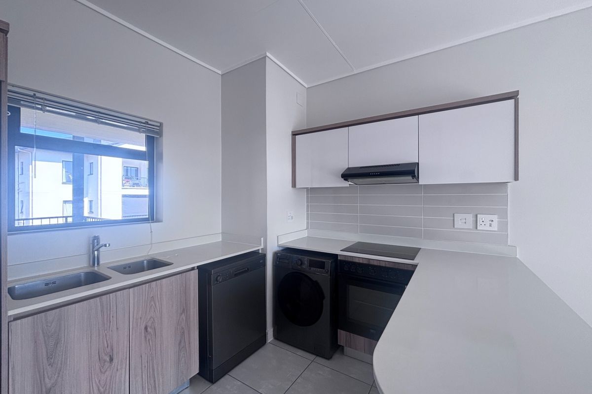 Modern kitchen featuring sleek cabinetry, stone countertops, integrated oven, electric hob, extractor fan, and a double basin sink with tiled flooring.
