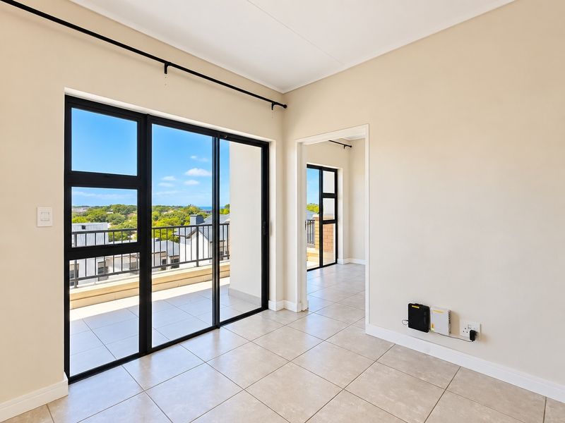 Bright and spacious living area featuring neutral tiled flooring and large black aluminium sliding doors that open onto a private balcony with scenic views.