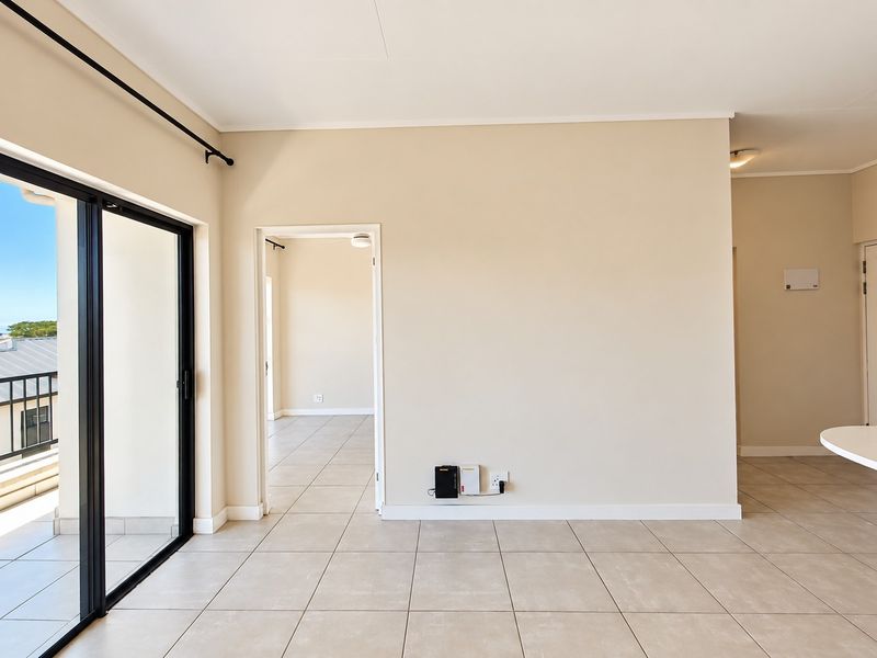 A bright, open-plan living area featuring neutral tiled flooring, clean walls, and a large sliding glass door leading to an outdoor balcony.