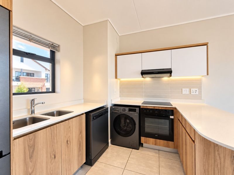 Modern kitchen featuring wood-grain cabinetry, stone countertops, integrated appliances, and under-cabinet lighting, offering a clean and functional workspace.