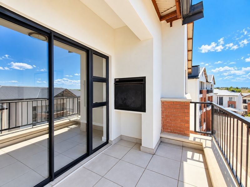 A spacious covered balcony featuring tiled flooring, a built-in braai, and a metal balustrade, offering a clean and modern outdoor entertainment space.