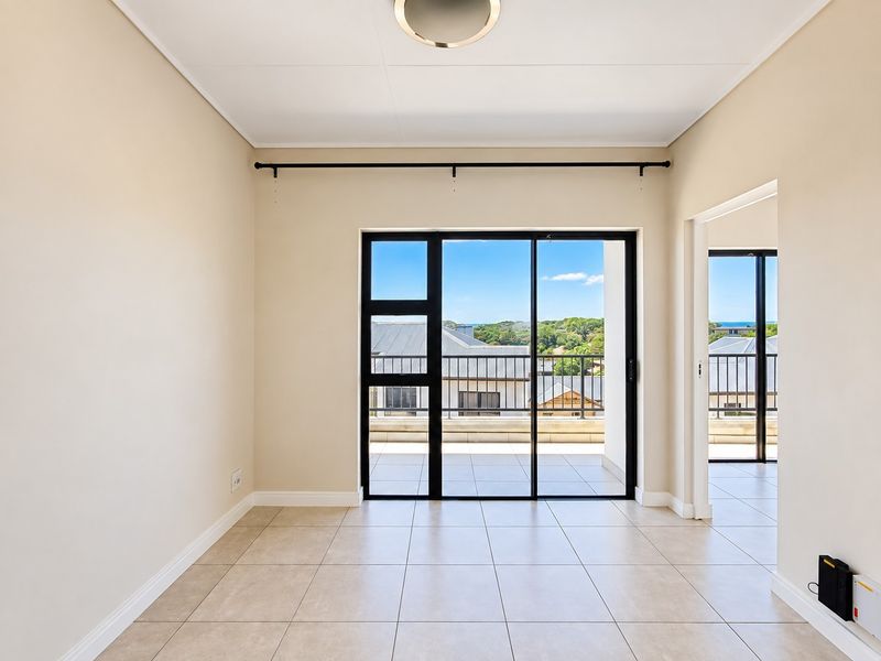 A bright, empty living area featuring neutral tiled flooring and a large sliding glass door that opens onto a balcony with scenic views.