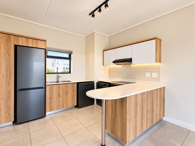 Modern kitchen featuring wood-finish cabinetry, stone countertops, integrated appliances, and sleek track lighting, offering a clean and functional culinary space.