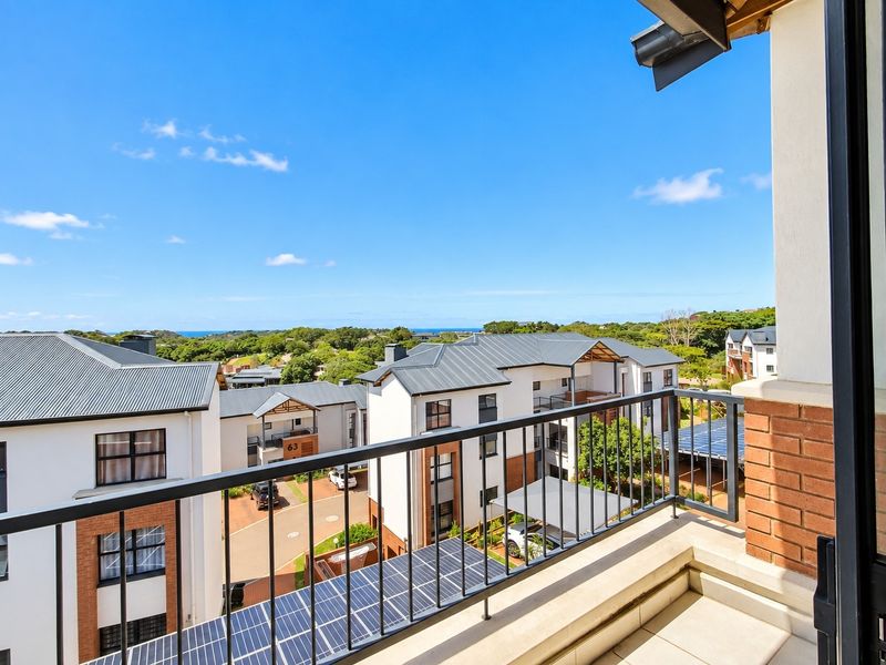 A clean, modern balcony with a metal balustrade and tiled flooring, offering an elevated view of the surrounding apartment complex and landscape.
