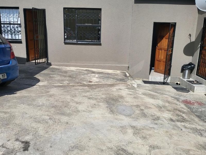 Exterior view of an apartment entrance featuring a concrete driveway, security gates, and security bars on the windows.