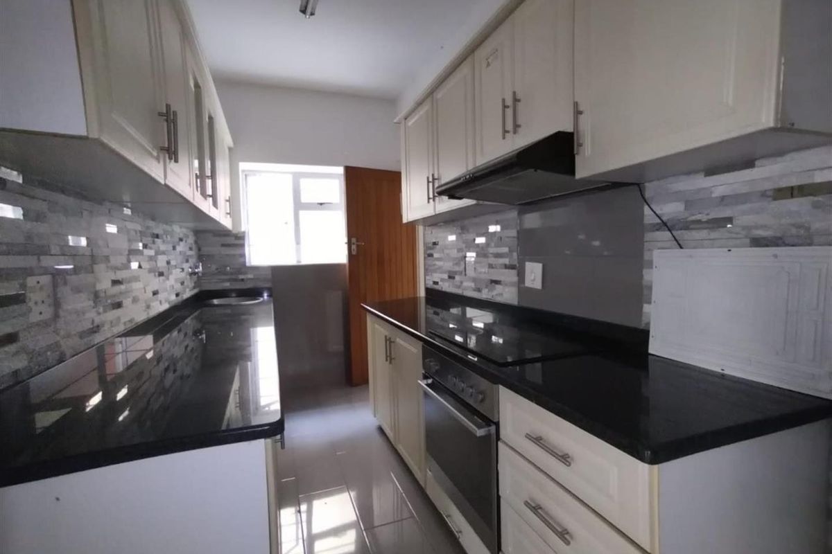 A clean, modern galley-style kitchen featuring granite countertops, built-in oven, electric hob, extractor fan, and ample cabinetry with a tiled backsplash.