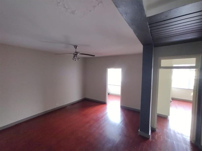 An empty living room featuring hardwood flooring, a ceiling fan, and an archway leading to an adjacent space.
