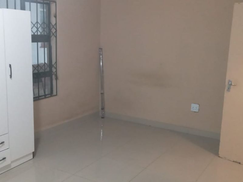 A simple bedroom featuring tiled flooring, a security gate on the window, and neutral wall finishes.