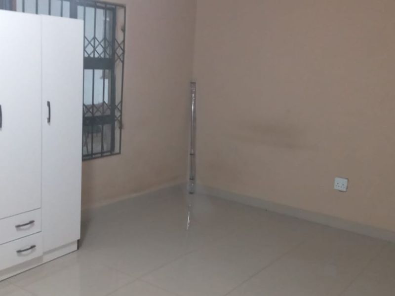 A simple, neutrally painted bedroom featuring tiled flooring and a window with security bars, offering a blank canvas for personalization.
