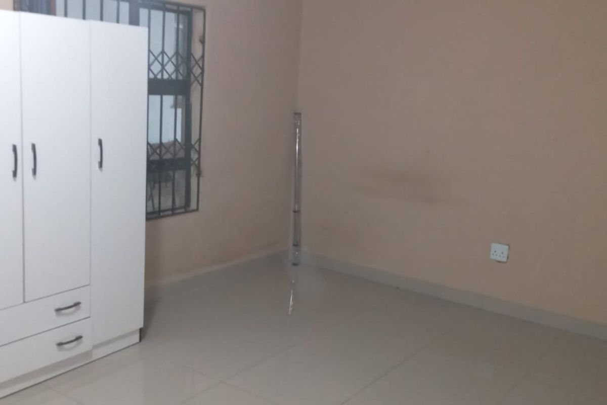 A simple, neutrally painted bedroom featuring tiled flooring and a window with security bars, offering a blank canvas for personalization.
