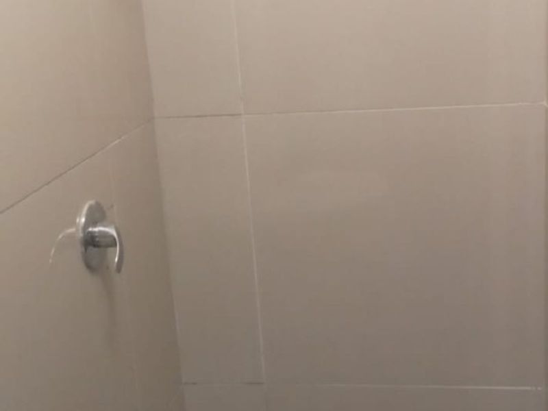 A compact shower enclosure featuring neutral wall tiling, mosaic floor tiles, and a wall-mounted shower fixture.