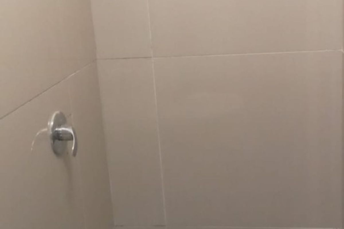 A compact shower enclosure featuring neutral wall tiling, mosaic floor tiles, and a wall-mounted shower fixture.