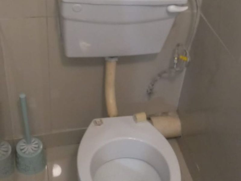 A functional bathroom featuring a standard white toilet and neutral ceramic wall and floor tiling.