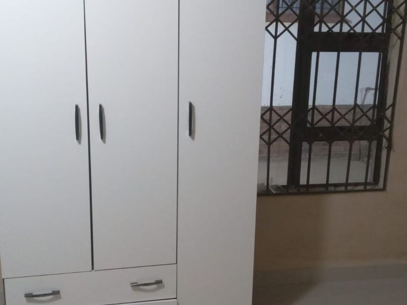 A bedroom interior featuring a white wardrobe and windows fitted with security bars.