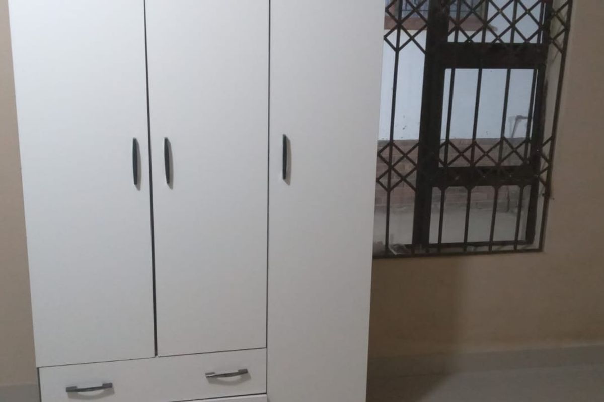 A bedroom interior featuring a white wardrobe and windows fitted with security bars.