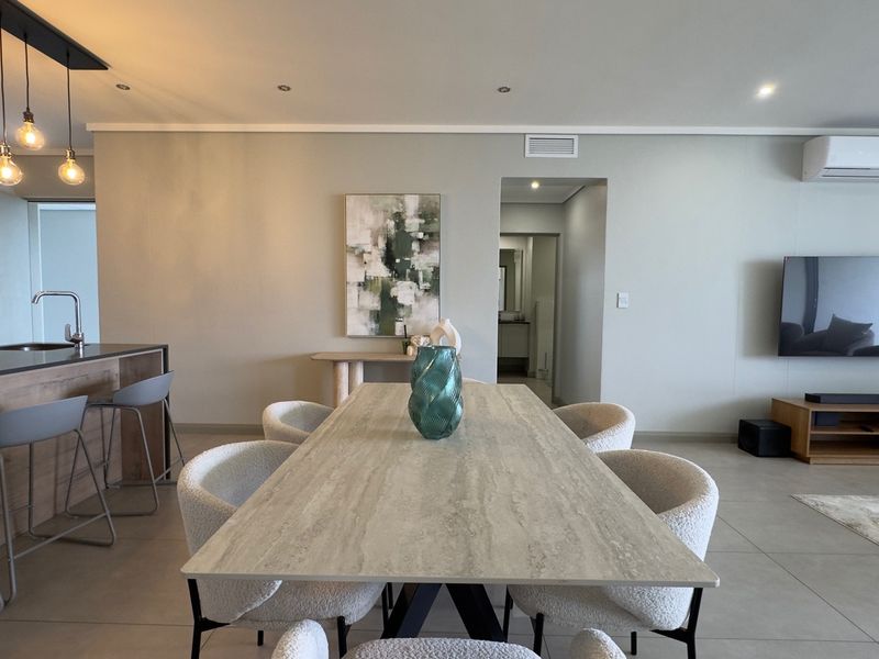 Modern open-plan living and dining area featuring tiled floors, recessed lighting, ducted air conditioning, and a functional kitchen island with sink.