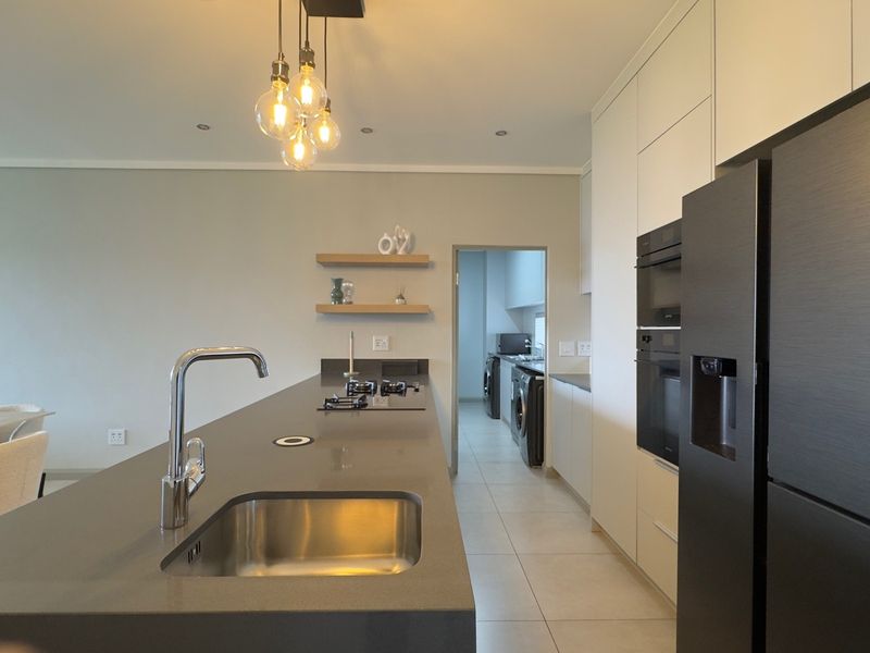 Modern kitchen featuring a large island with stone countertops, integrated appliances, sleek cabinetry, and a separate scullery area.