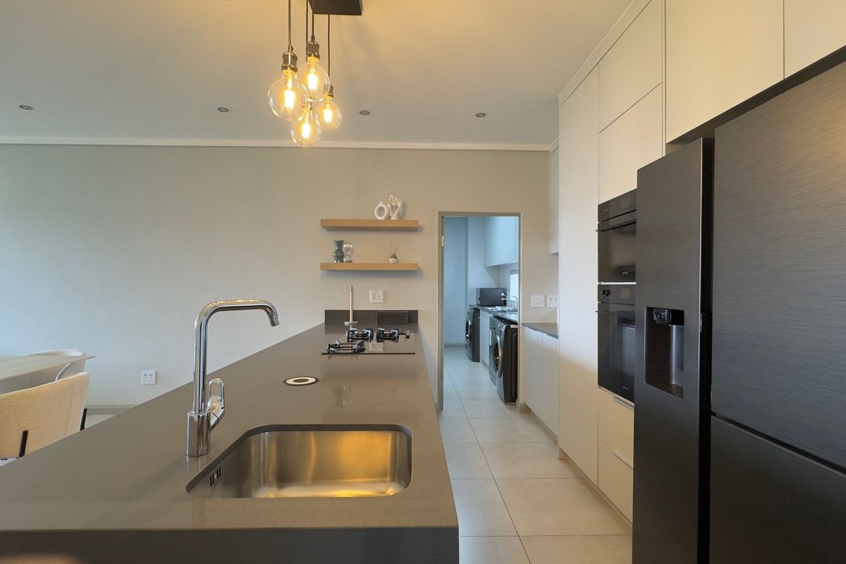 Modern kitchen featuring a large island with stone countertops, integrated appliances, sleek cabinetry, and a separate scullery area.