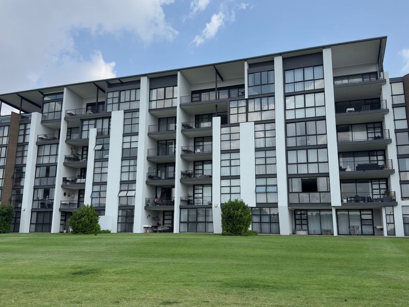 A view of the rear elevation of a modern apartment complex featuring multiple balconies, large glass windows, and a well-maintained lawn area.