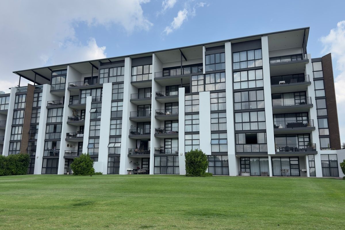 A view of the rear elevation of a modern apartment complex featuring multiple balconies, large glass windows, and a well-maintained lawn area.