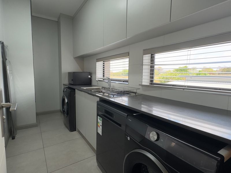 Modern laundry room featuring sleek built-in cabinetry, stone countertops, a stainless steel sink, and tiled flooring with integrated appliance spaces.