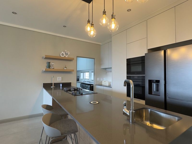 Modern kitchen featuring stone countertops, integrated appliances, gas hob, and sleek cabinetry with stylish pendant lighting and a functional breakfast bar.