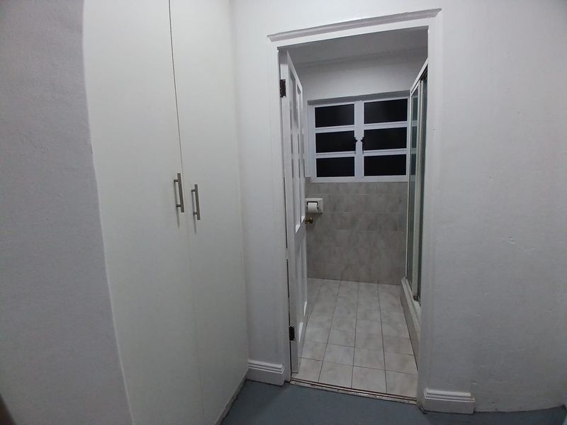 A functional bathroom featuring a shower enclosure, tiled finishes, and built-in storage cupboards in the adjacent hallway area.